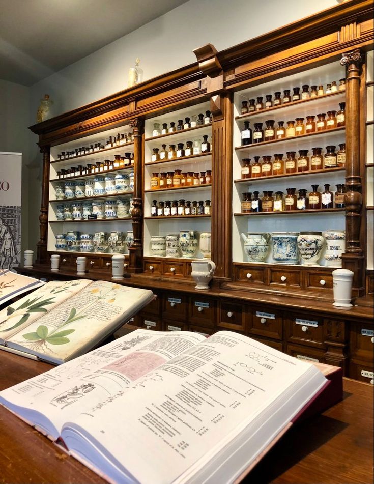 an open book sitting on top of a wooden table next to shelves filled with bottles