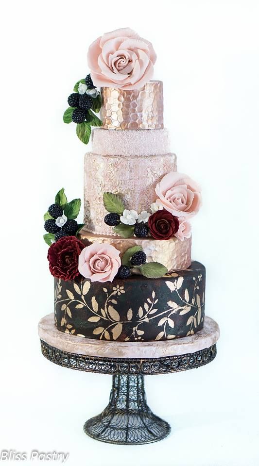 a three tiered cake with roses on top is decorated in gold, black and pink