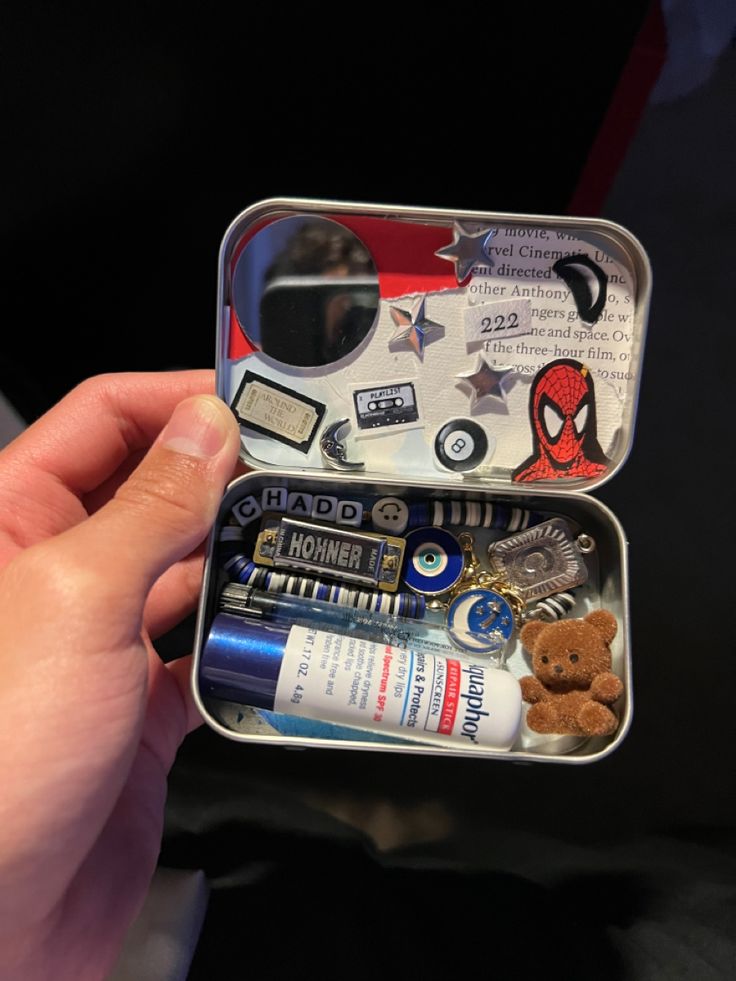 someone is holding an open tin with various items in it and there are other things inside the tin