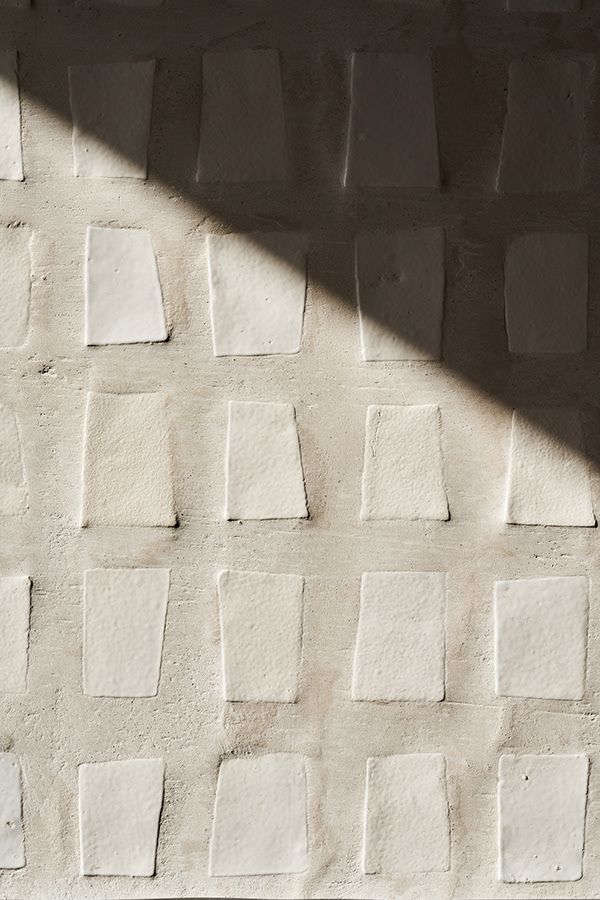 a white brick wall with small squares on it and a shadow cast by the light