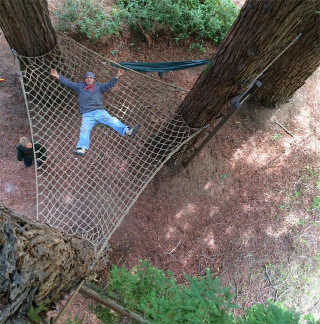 a man is laying on a hammock between two trees in the woods with his arms outstretched