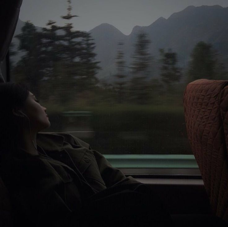 a woman sitting on a train seat looking out the window at mountains and trees in the distance