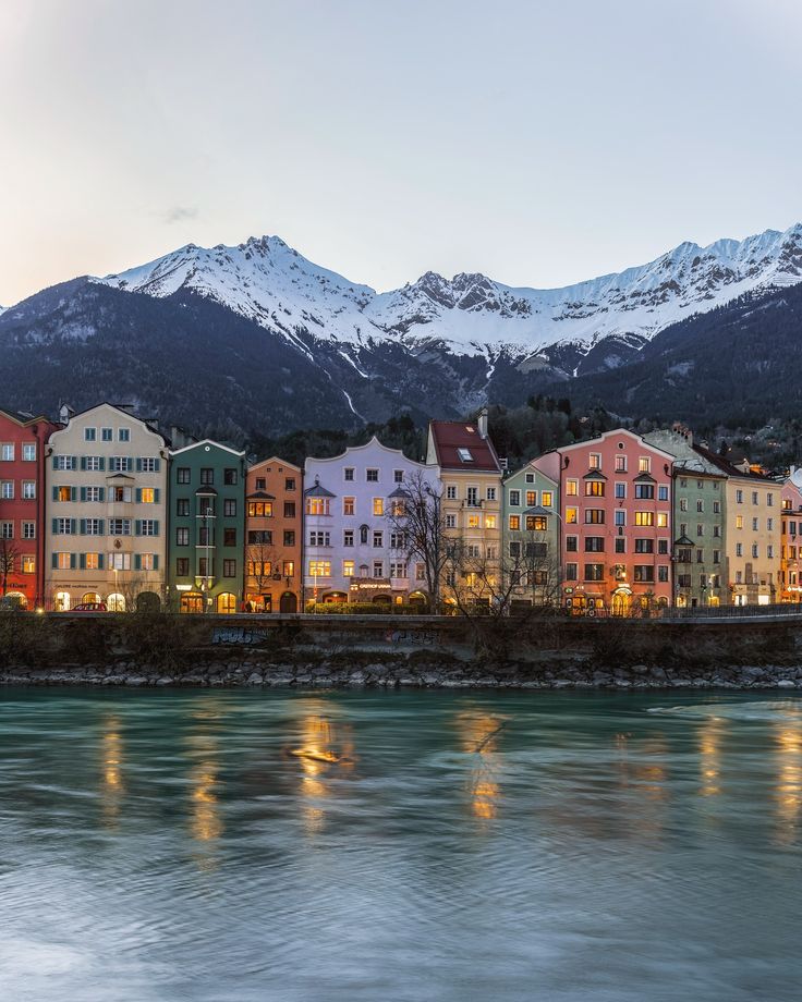 some buildings are lit up by the water and mountains in the backgrouds