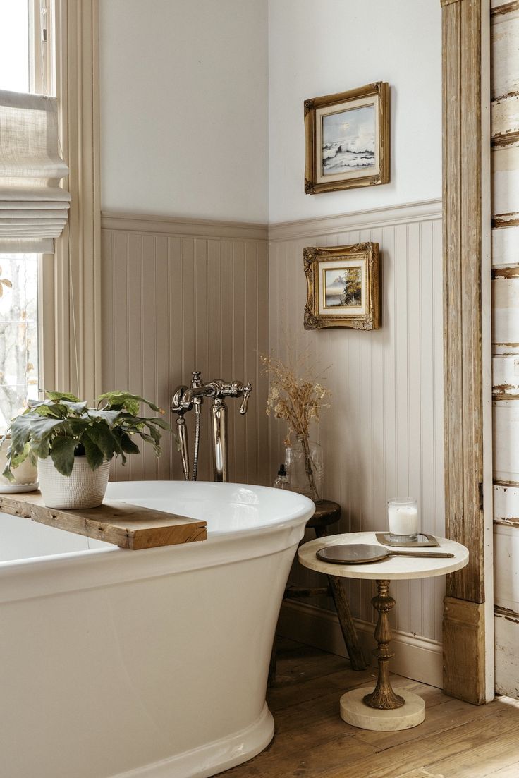 a white bath tub sitting in a bathroom next to a table with flowers on it