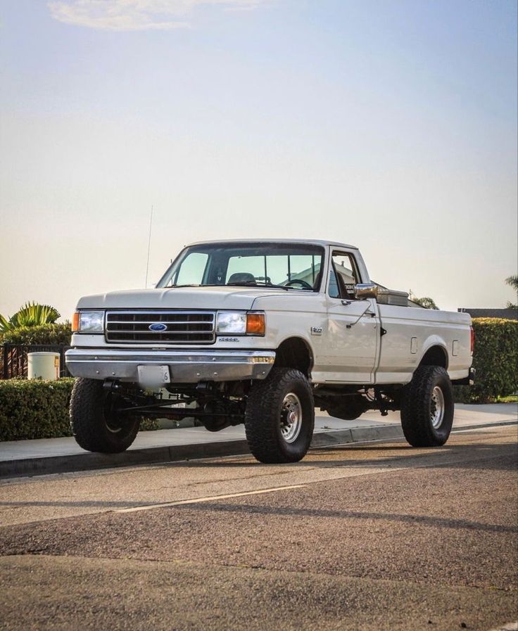 a large white truck parked on the side of a road next to a bushbery