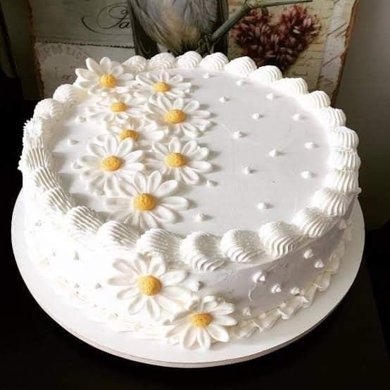 a white cake with daisies on it sitting on a table next to a vase