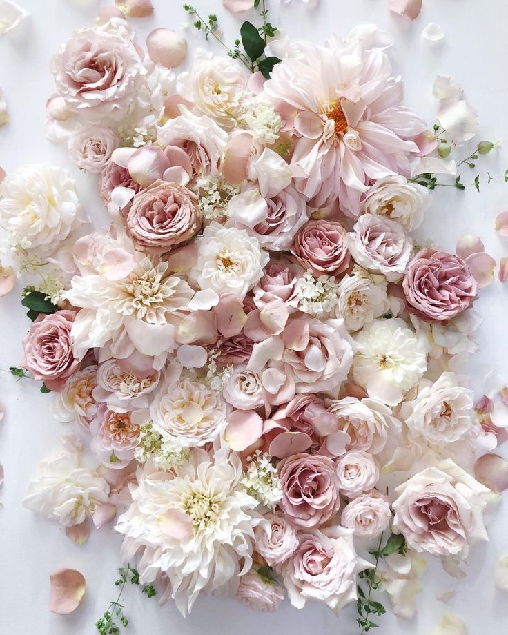 an arrangement of pink and white flowers on a white surface with greenery around it