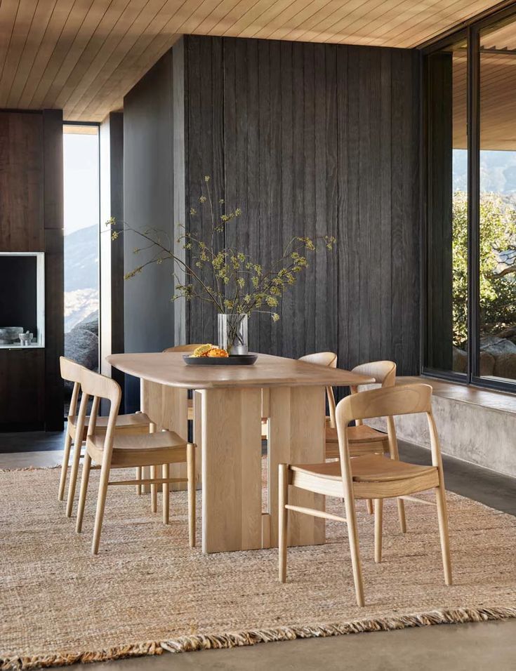 a dining room table with chairs and a vase on it in front of a window