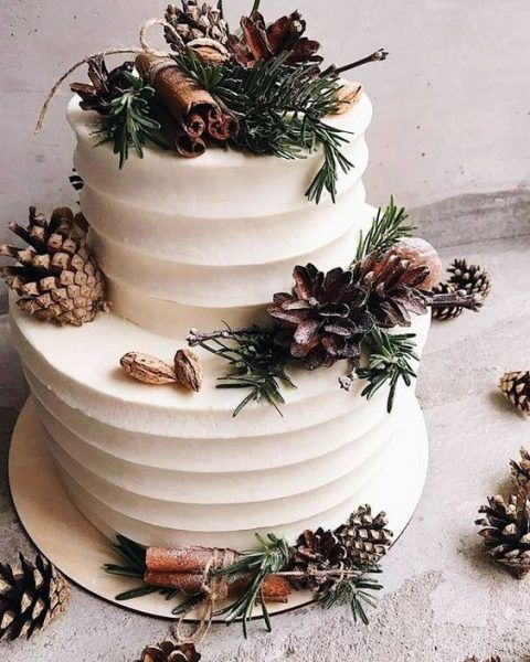 a three tiered white cake with pine cones and greenery on the top layer