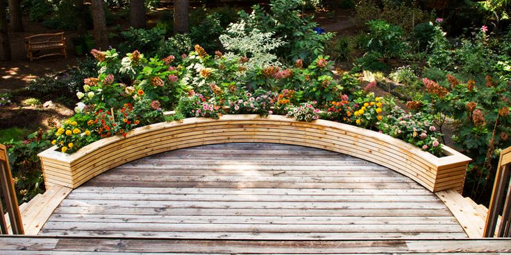 a wooden bench sitting on top of a lush green hillside next to trees and flowers