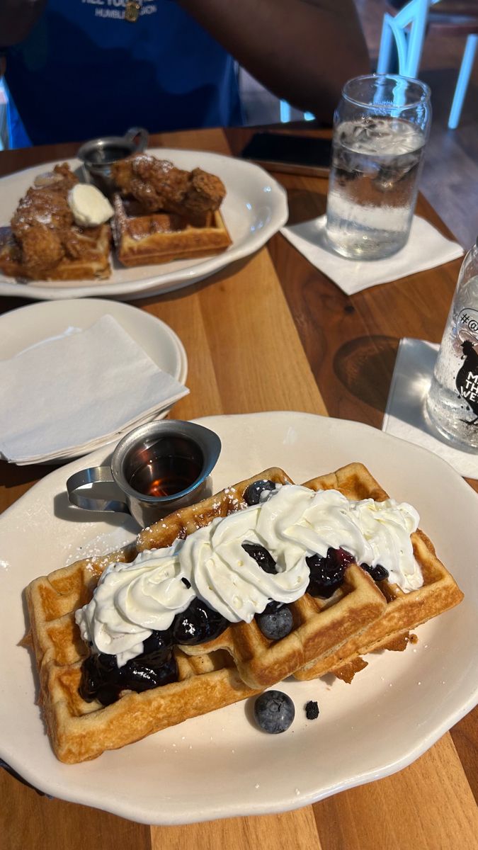 two waffles with whipped cream and blueberries on them sitting on a table