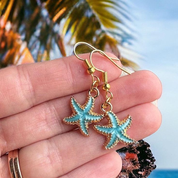 These cute custom starfish earrings will transport you right to the beach!  With dainty gold accents and gorgeous Caribbean blue colors, these beachy earrings perfectly capture the unparalleled beauty of the ocean. Our sky blue starfish earrings measure approximately 1 1/4" in length - lightweight and comfortable for everyday wear, yet elegant enough for a classy evening out.  We've paired these starfish pendants with 14 karat gold earring hooks for a luxurious look and feel. Perfect for a destination beach wedding or Caribbean cruise vacation! All of our ocean-inspired jewelry radiates the warmth and shimmer of the sea and these summery blue starfish earring are no exception. Ideal for beach lovers or sea life animal enthusiasts, our iridescent starfish earrings would make a wonderful gif Gold Starfish Jewelry For Vacation, Beachy Gold Jewelry With Starfish Charm, Gold Jewelry With Star Charm For Vacation, Gold Star Charm Jewelry For Vacation, Beach Jewelry With Starfish Charm, Ocean-inspired Star Charm Jewelry For Beach, Ocean-inspired Beach Jewelry With Star Charm, Summer Gold Jewelry With Star Charm, Summer Ocean-inspired Jewelry With Star Charm