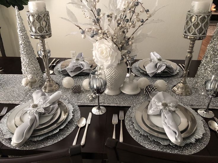 the table is set with silver and white plates, silver napkins, flowers, and candlesticks