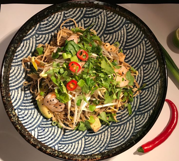 a blue and white bowl filled with food on top of a table next to red peppers