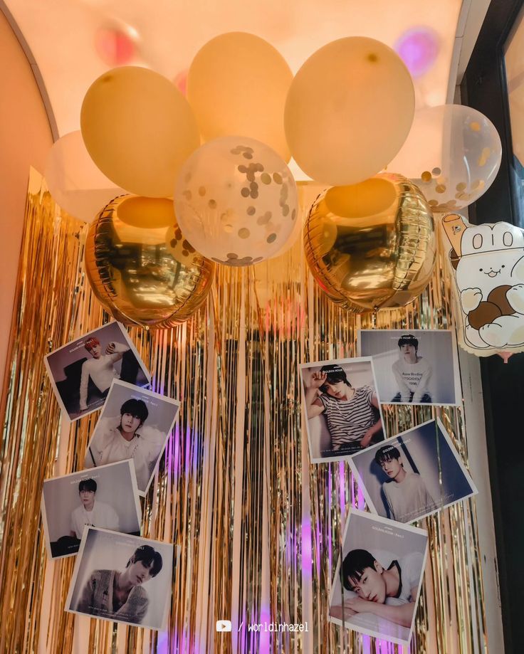 balloons and pictures hanging from the ceiling in front of a wall with gold streamers