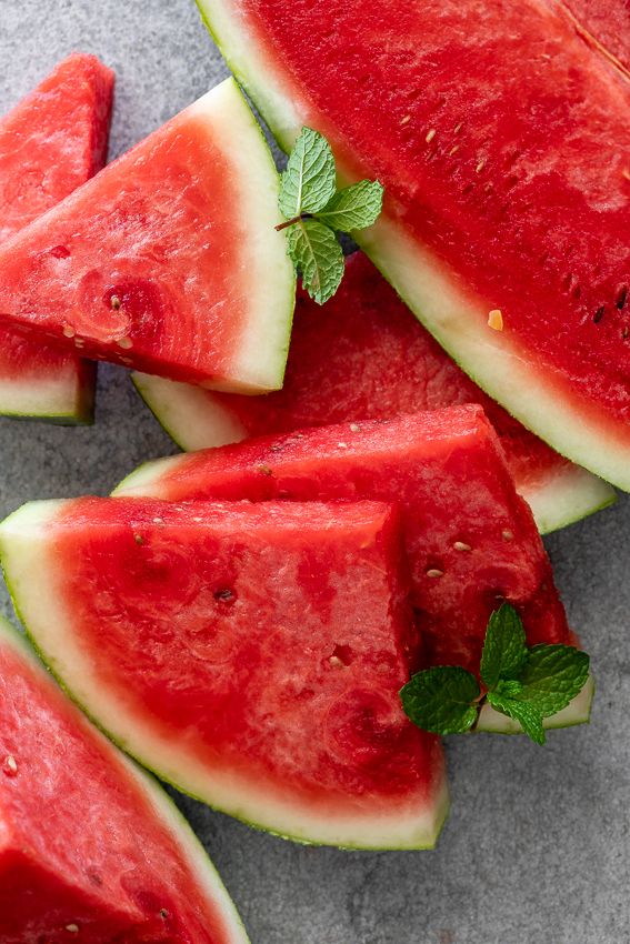 slices of watermelon and mint on a gray surface with green leafy garnish