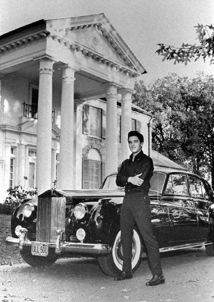 a black and white photo of a man standing next to a car in front of a house