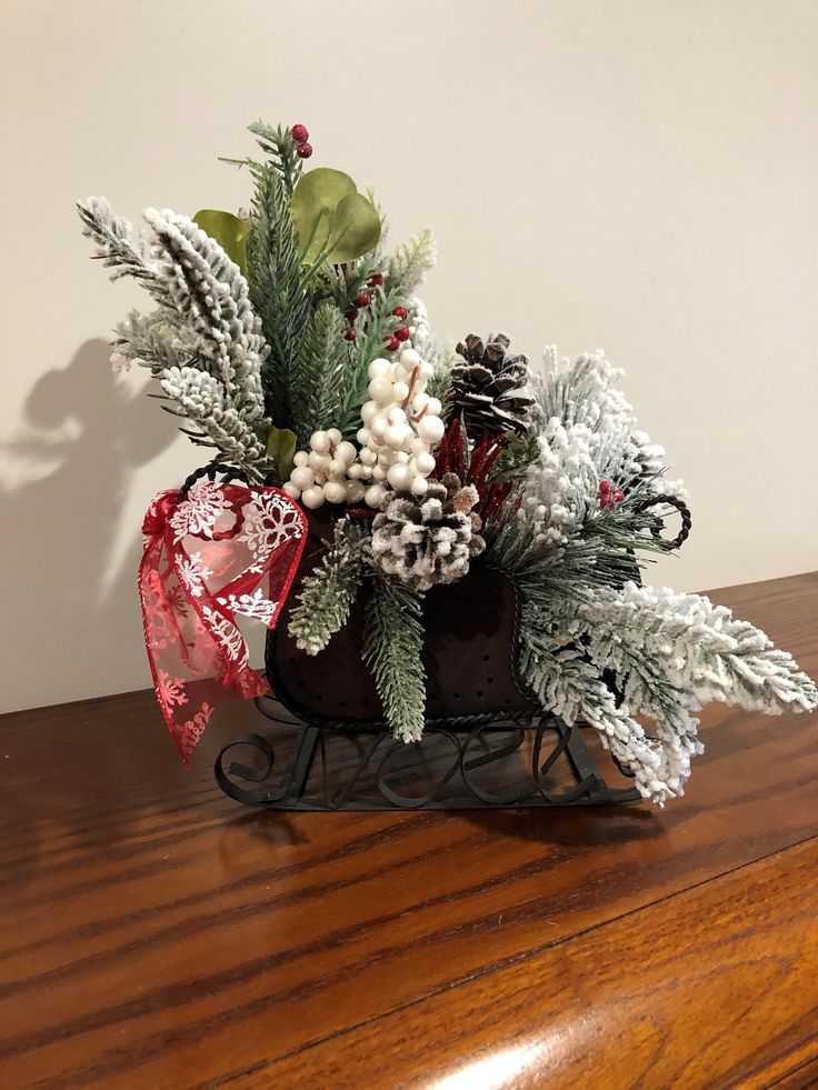 a small sleigh filled with pine cones, berries and greenery on top of a wooden table