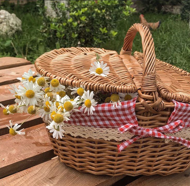 a wicker basket filled with daisies sitting on top of a wooden picnic table