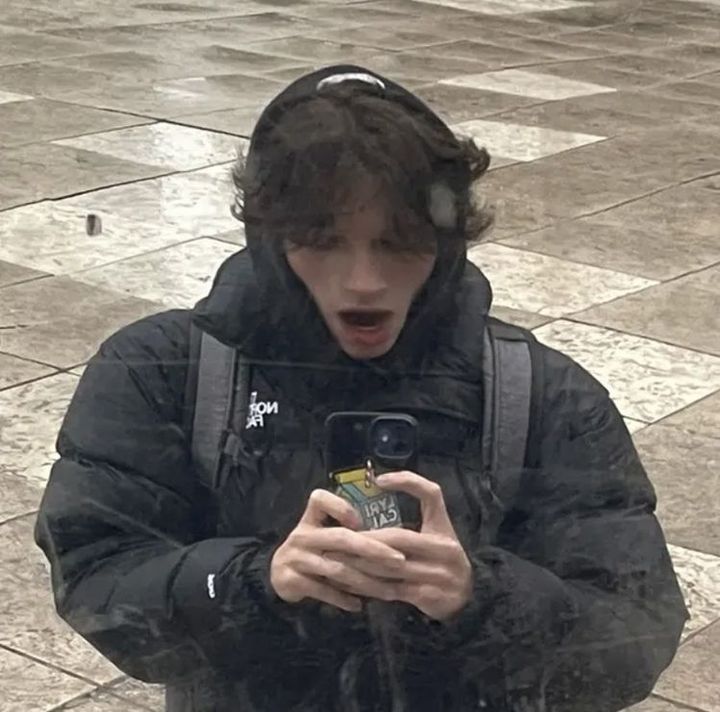 a young man standing in the rain looking at his cell phone and making a face