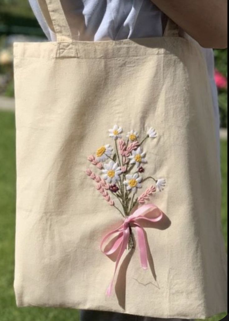 a person holding a tote bag with flowers on the front and pink ribbon around it