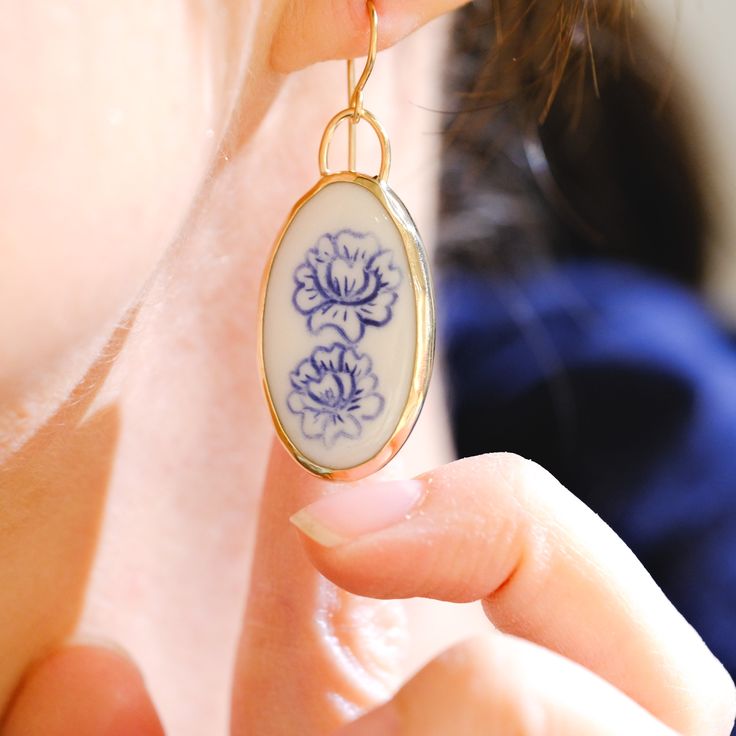 a close up of a person holding a pair of earrings with blue flowers on it