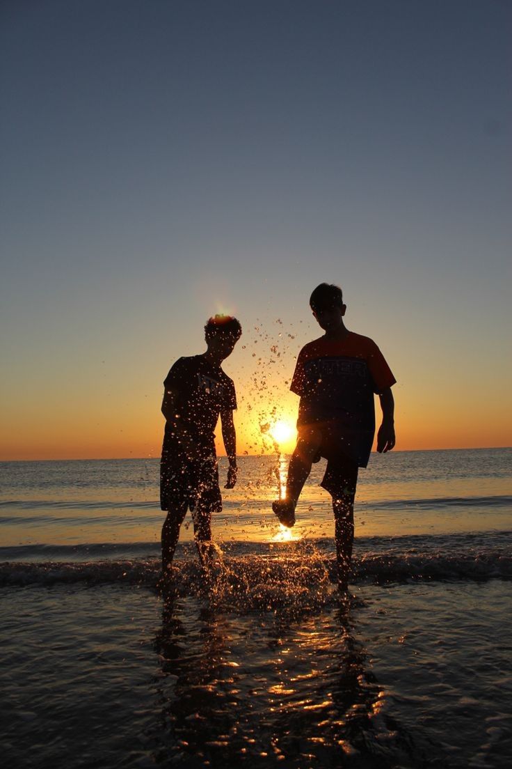 two people standing on the beach at sunset with water splashing from their feet in the air