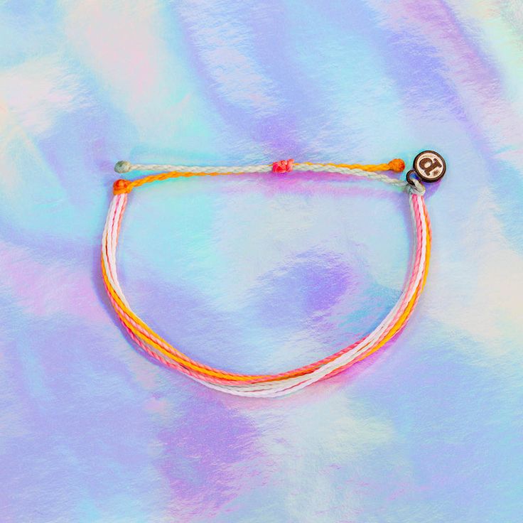 an orange and white string bracelet with a button on it's end, sitting on a pastel background