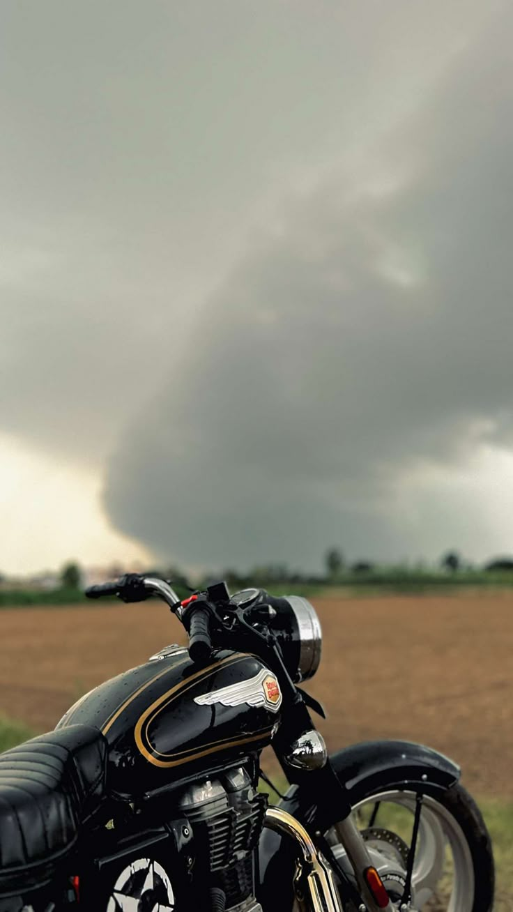 a motorcycle parked on the side of a road in front of a field with storm clouds