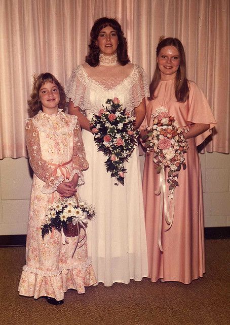 three women in dresses standing next to each other with flowers on their bouquets and holding bridal gowns