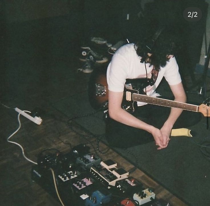 a person sitting on the floor with a guitar in front of them and other electronics