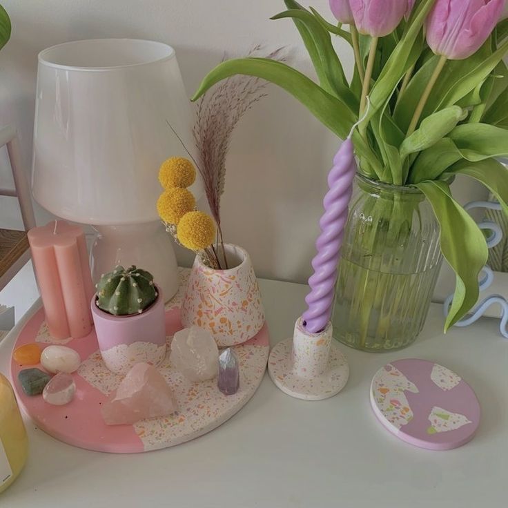 a vase with flowers and other items on a table next to a lamp, candle holder