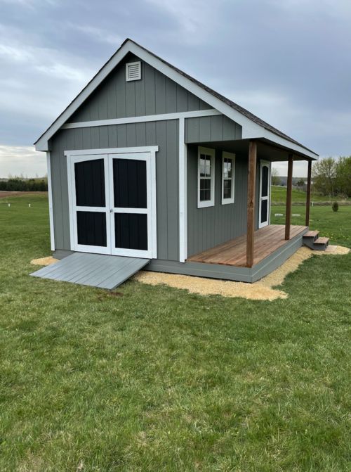 a small gray shed sitting on top of a lush green field next to a wooden deck