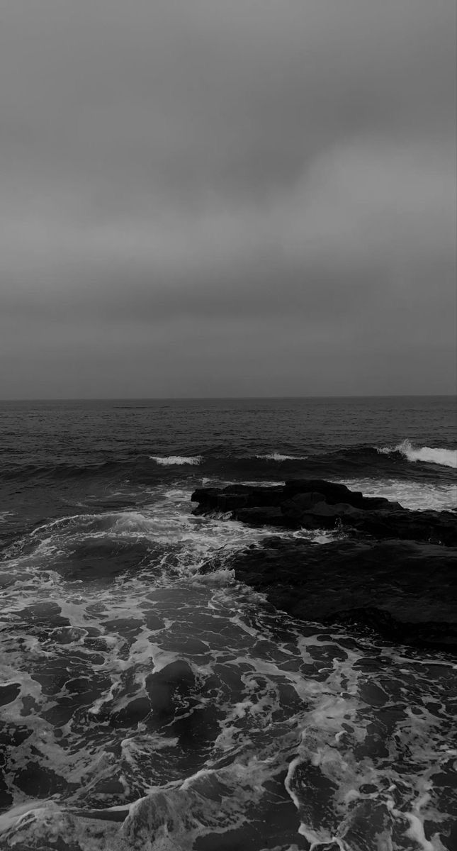 a black and white photo of the ocean with waves crashing on it's shore