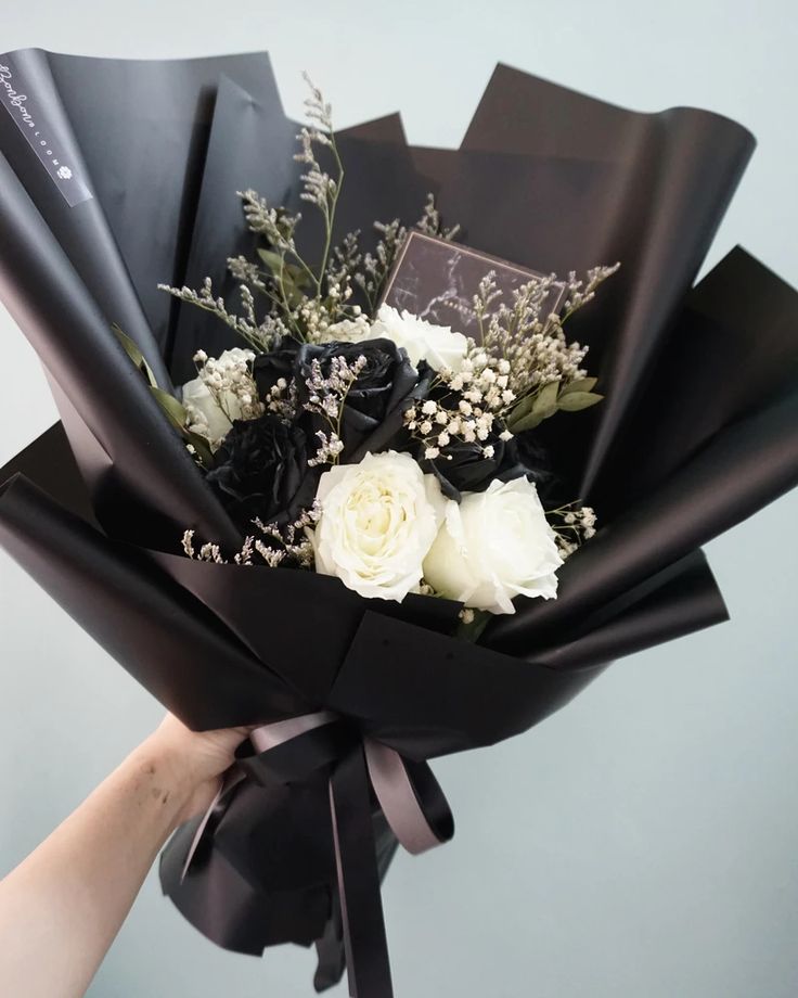 a bouquet of white and black flowers is wrapped in black paper with ribbon around it