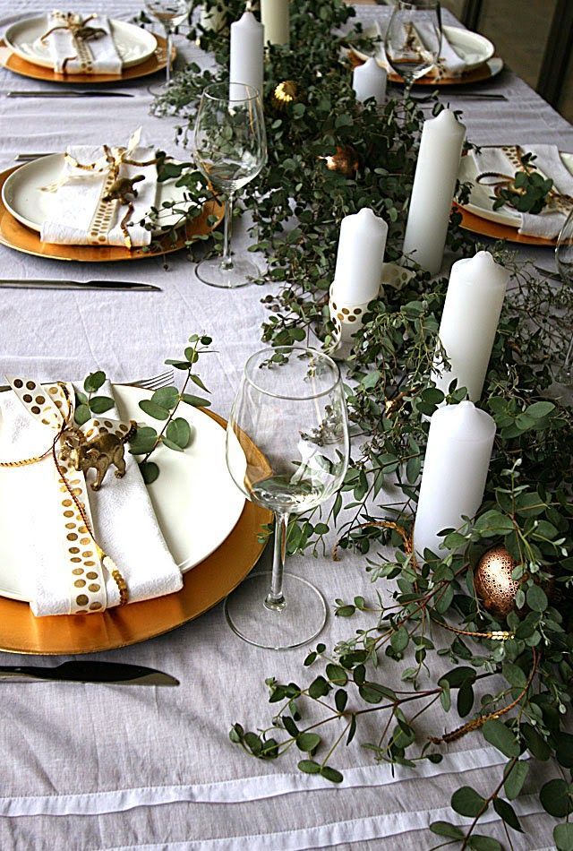 the table is set with white and gold plates, silverware, greenery and candles