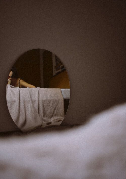 the reflection of a person lying in bed with their head on a pillow, looking into a round mirror