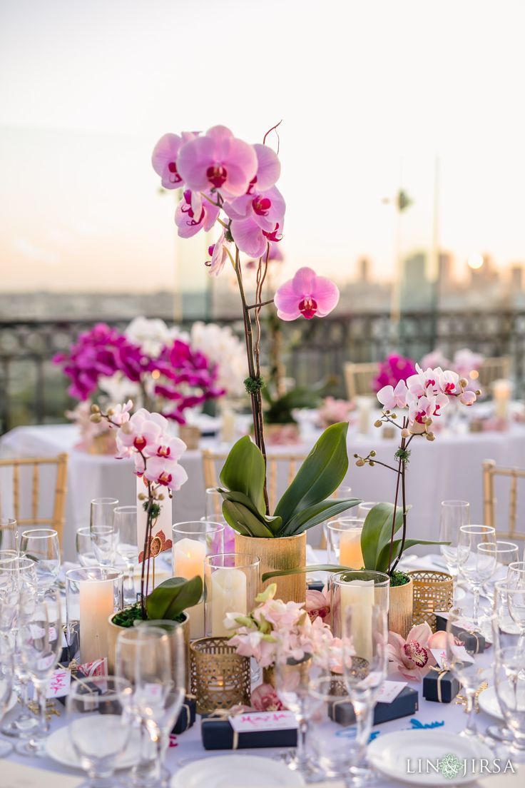 the table is set with pink and white flowers in vases, candles, and wine glasses