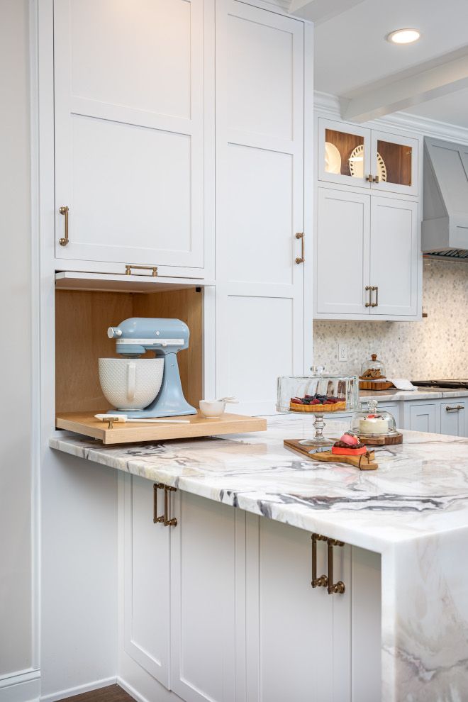 a kitchen with white cabinets and marble counter tops, including a mixer in the center