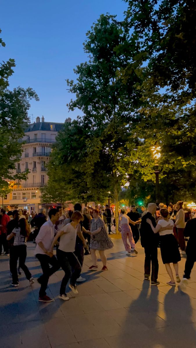 a group of people dancing around in the street at night with buildings in the background