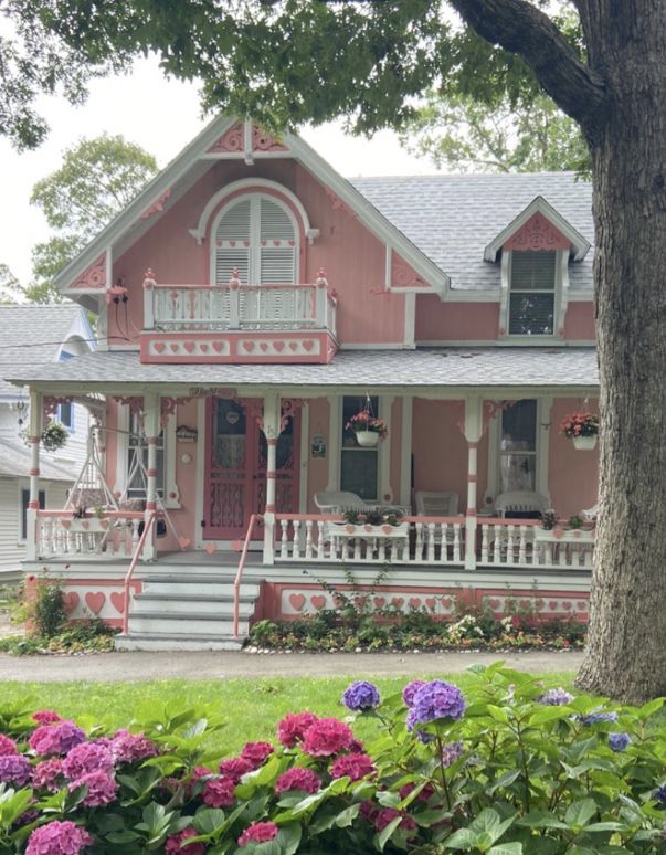 a pink house with flowers in front of it and trees around the porchs on both sides