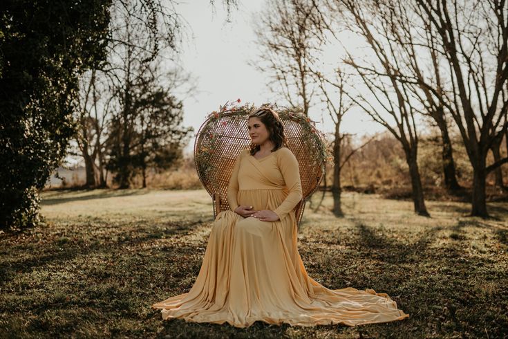 a pregnant woman sitting in a wicker chair with her hands on her belly and holding an umbrella