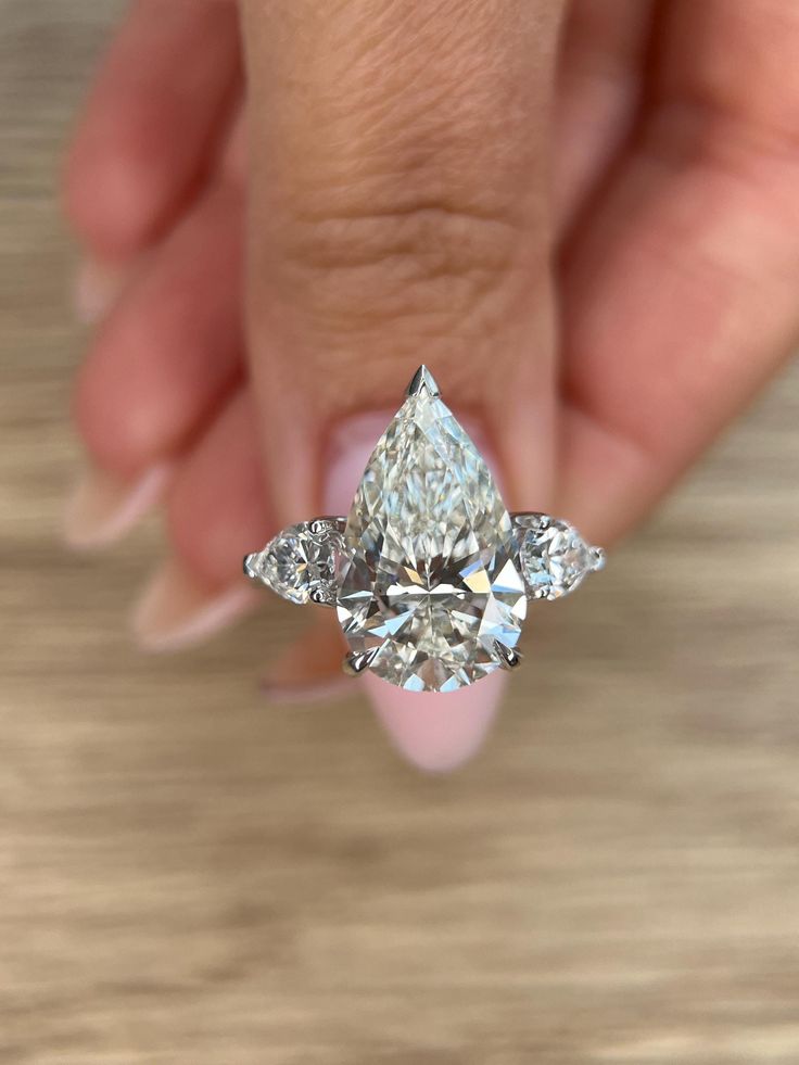 a woman's hand holding an engagement ring with three pear shaped diamonds