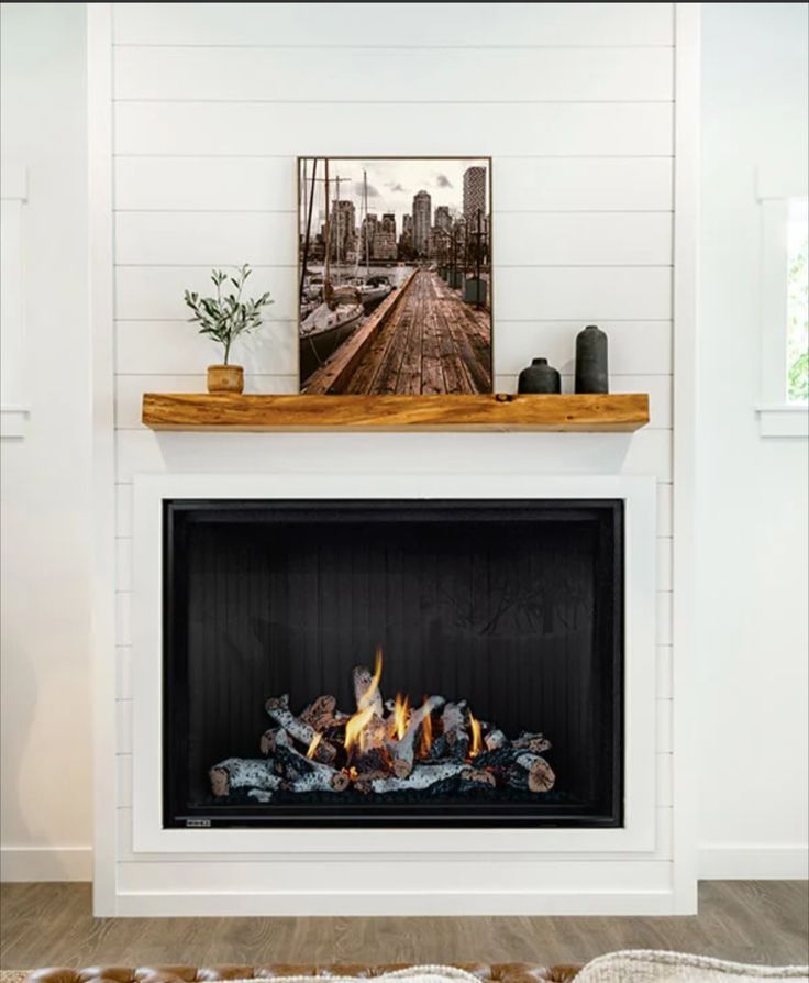 a fire place in the middle of a living room with white walls and wood flooring