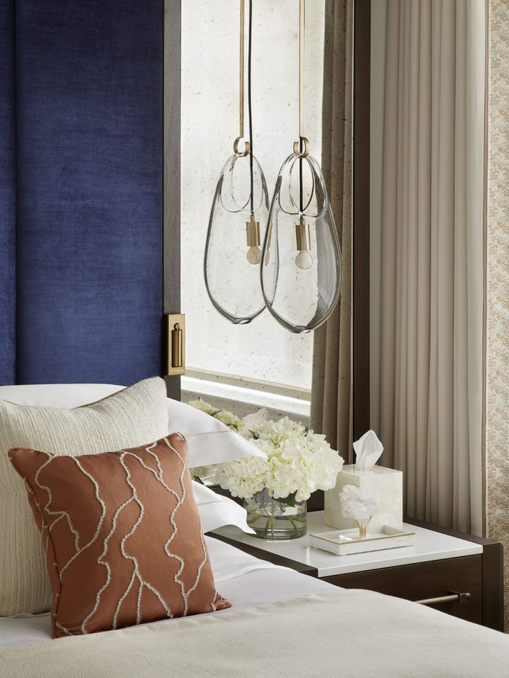 a bedroom with blue walls, white bedding and two chandeliers hanging from the ceiling