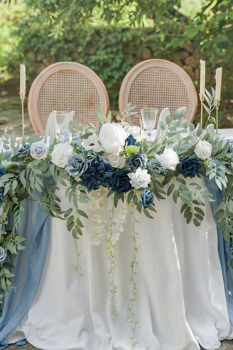 the table is set with blue and white flowers, greenery, candles and chairs