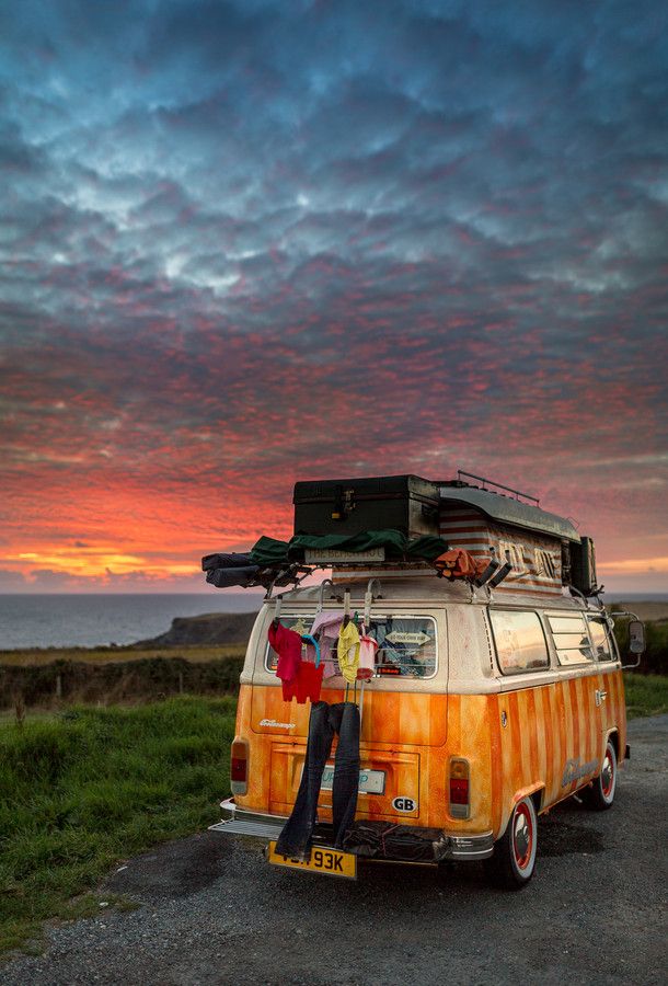 an old vw camper van parked on the side of a road with luggage strapped to it's roof