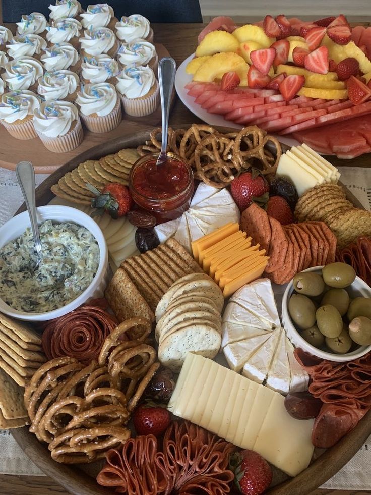 an assortment of cheeses, crackers and fruit on a platter with dips