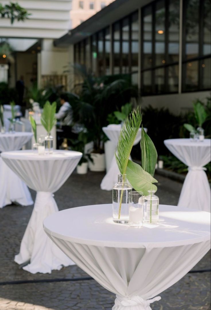 tables with white tablecloths and green plants in vases on the side walk