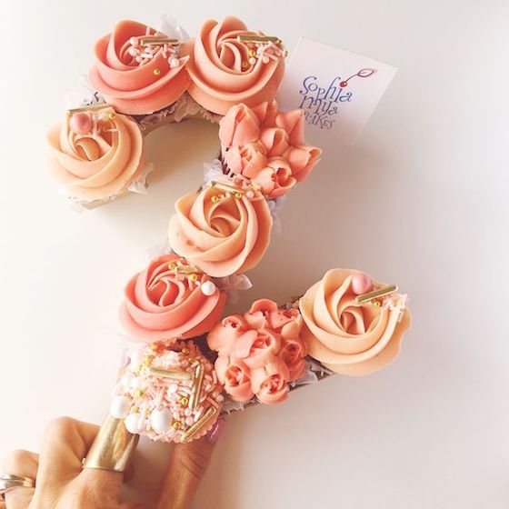 a person is holding some cupcakes with icing and flowers on them in front of a white background